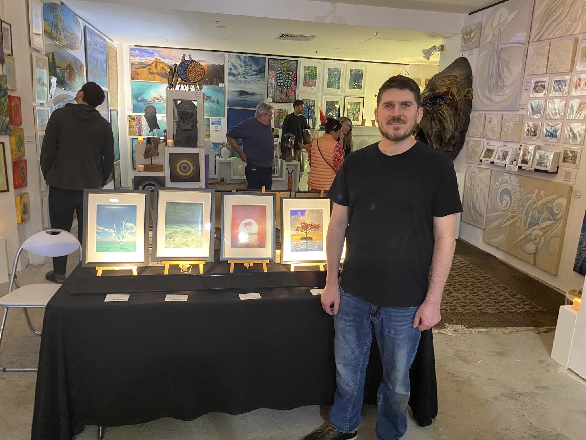 Jay Salton standing in front of four framed works at his Gold Coast exhibition