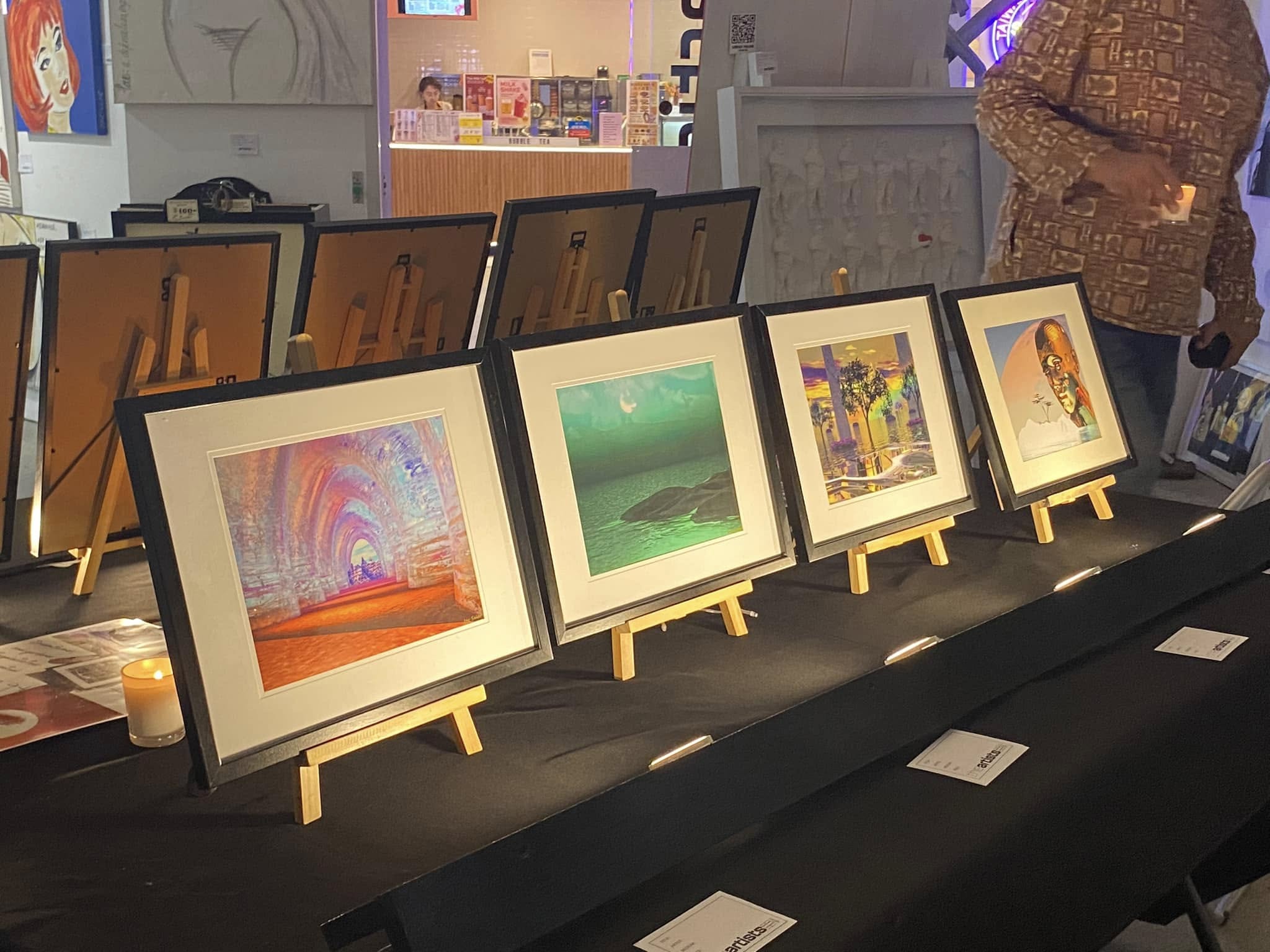 Four colourful framed artworks by Jay Salton arranged on tabletop easels